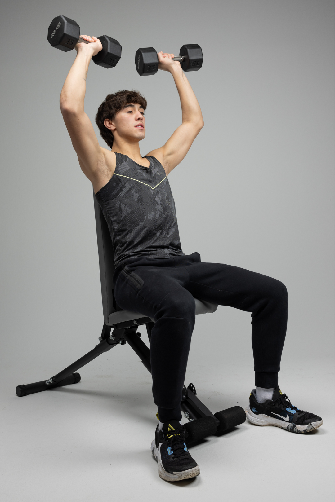 Young man sitting in weight bench lifting set of octo dumbbells by Rage Fitness in shoulder press